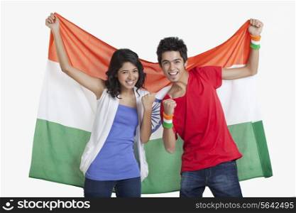 Portrait of happy young friends cheering while holding Indian flag over white background