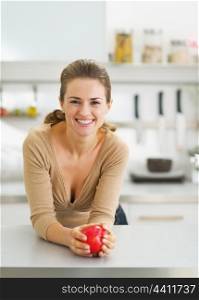 Portrait of happy young housewife with apple in modern kitchen