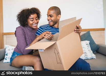 Portrait of happy young latin couple opening a package at home. Delivery, shipping and postal service concept.