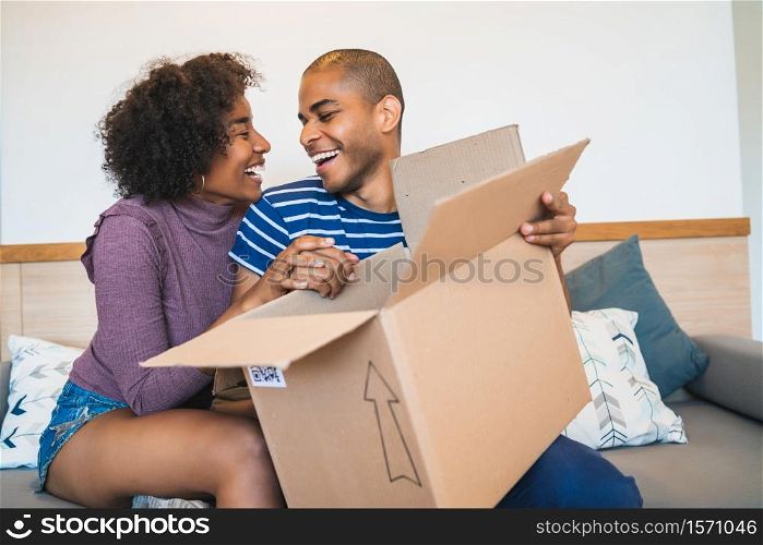 Portrait of happy young latin couple opening a package at home. Delivery, shipping and postal service concept.