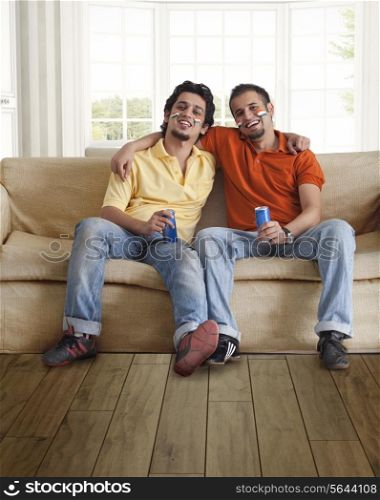 Portrait of happy young male friends sitting comfortably on sofa with tin cans