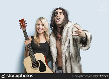 Portrait of happy young man gesturing with woman holding guitar against light blue background