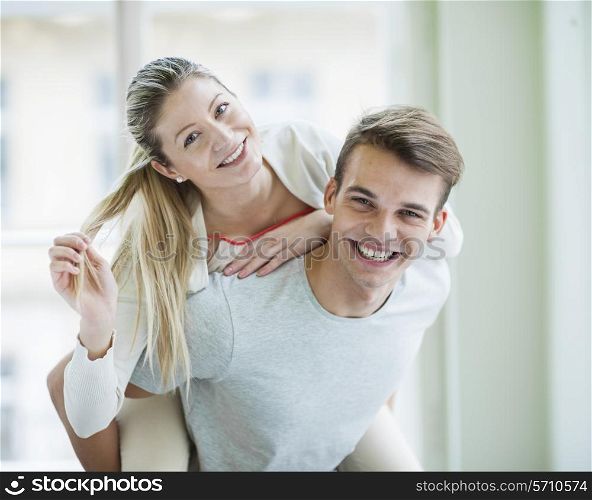 Portrait of happy young man giving piggyback ride to woman at home