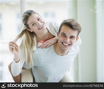 Portrait of happy young man giving piggyback ride to woman at home