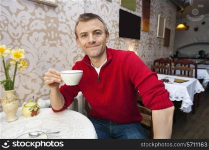 Portrait of happy young man holding coffee cup at cafe