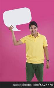 Portrait of happy young man holding speech bubble over pink background