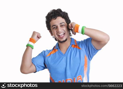 Portrait of happy young man in jersey cheering with clenched fist while answering phone call over white background