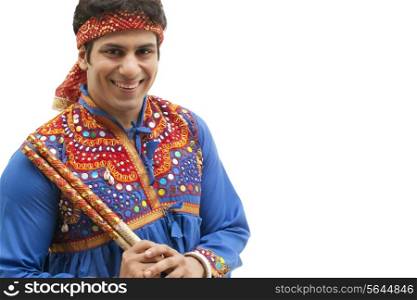 Portrait of happy young man in traditional wear holding dandiya isolated over white background