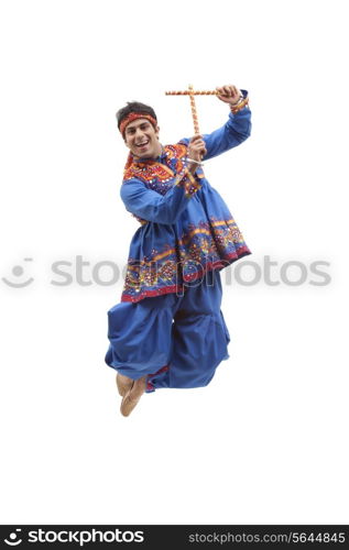 Portrait of happy young man in traditional wear jumping in mid air as he performs Dandiya Raas over white background