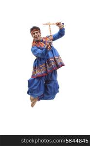 Portrait of happy young man in traditional wear jumping in mid air as he performs Dandiya Raas over white background