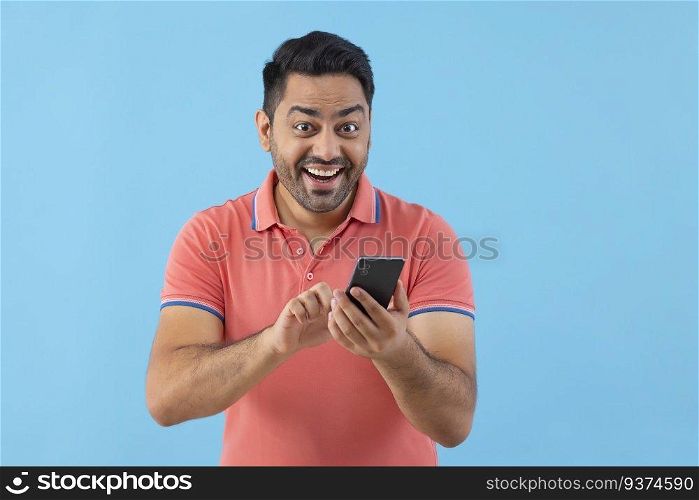 Portrait of happy young man looking at camera while using Smartphone