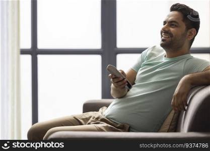 Portrait of happy young man watching television while sitting on sofa in living room