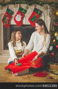 Portrait of happy young mother and cheerful daughter decorating Christmas presents