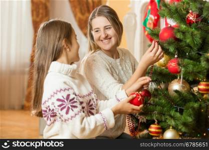 Portrait of happy young mother and daughter decorating Christmas tree