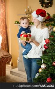 Portrait of happy young mother giving gift box to her baby at Christmas