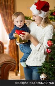 Portrait of happy young mother giving gift box to her baby boy at Christmas
