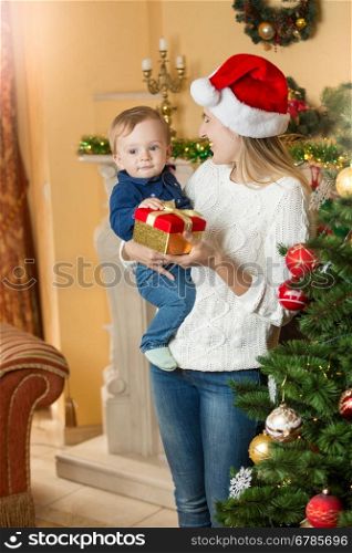 Portrait of happy young mother giving present to her baby son on Christmas at living room next to Christmas tree