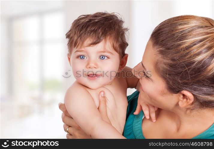 Portrait of happy young mother holding on hands cute little son and looking on him with great love, with pleasure spending time at home, enjoying motherhood