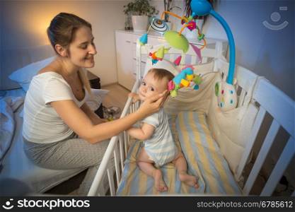Portrait of happy young mother looking at her baby in crib before going to sleep