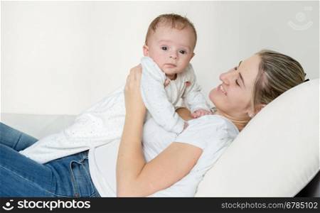 Portrait of happy young mother lying on bed and holding her 3 months old baby boy