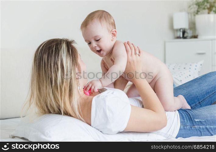 Portrait of happy young mother lying on bed and playing with baby