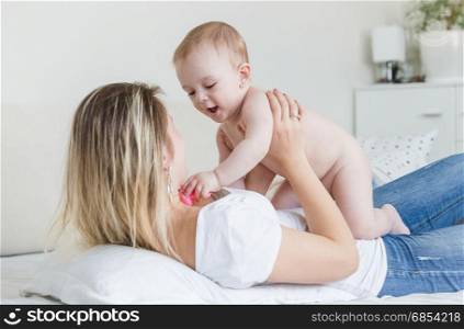 Portrait of happy young mother lying on bed and playing with baby