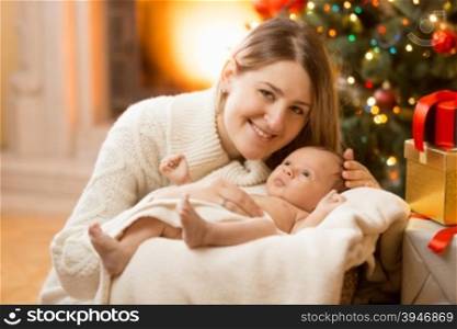 Portrait of happy young mother posing with newborn baby boy at house decorated for Christmas
