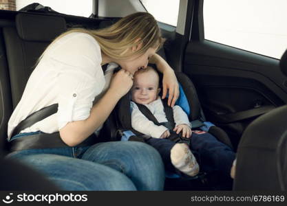 Portrait of happy young mother sitting on back seat with her baby