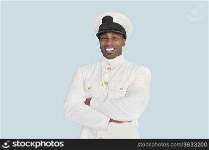 Portrait of happy young Navy officer with arms crossed standing over light blue background