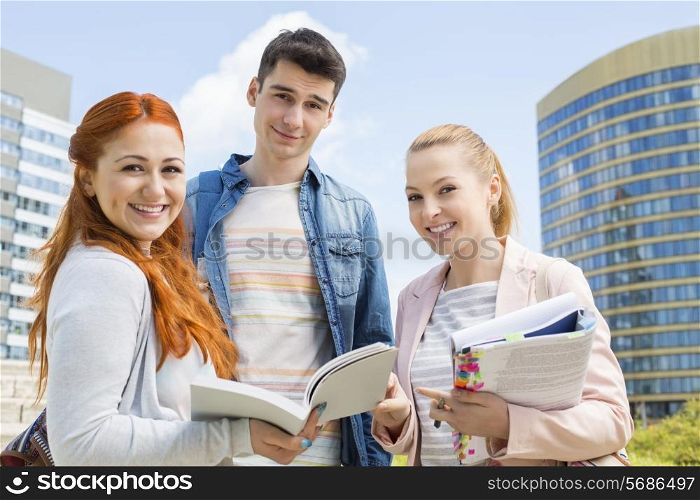 Portrait of happy young university students studying outdoors