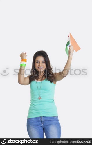 Portrait of happy young woman cheering while holding Indian flag over white background