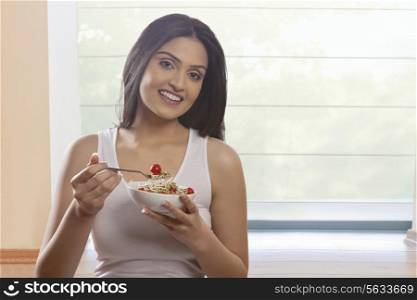 Portrait of happy young woman eating bean sprouts and cherry tomatoes