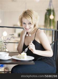 Portrait of happy young woman eating cake at cafe