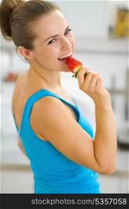Portrait of happy young woman eating strawberry in modern kitchen