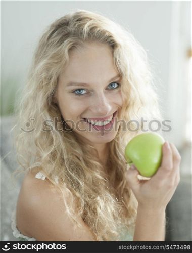 Portrait of happy young woman holding apple in house