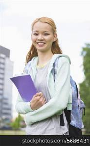 Portrait of happy young woman holding book at college campus