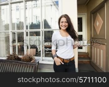 Portrait of happy young woman holding coffee cup in front of cafe