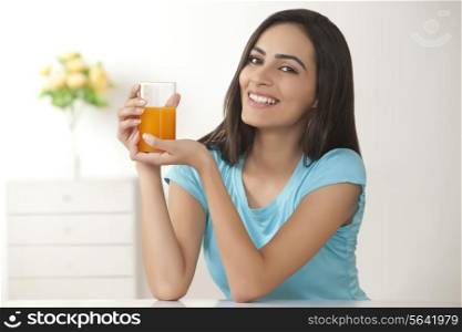 Portrait of happy young woman holding glass of fresh orange juice at home