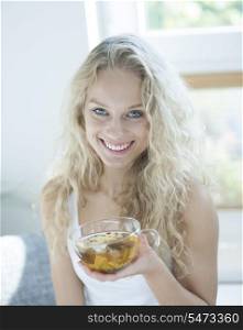 Portrait of happy young woman holding herbal tea cup in house