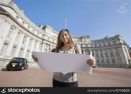 Portrait of happy young woman holding map against Admiralty Arch in London; England; UK