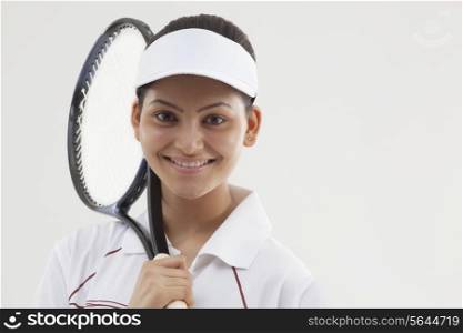 Portrait of happy young woman holding tennis racket isolated over gray background