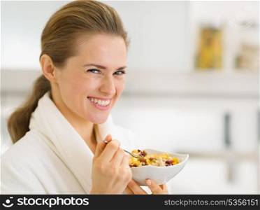 Portrait of happy young woman in bathrobe eating healthy breakfast