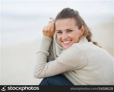 Portrait of happy young woman in sweater sitting on lonely beach