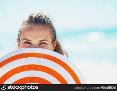Portrait of happy young woman in swimsuit hiding behind beach hat