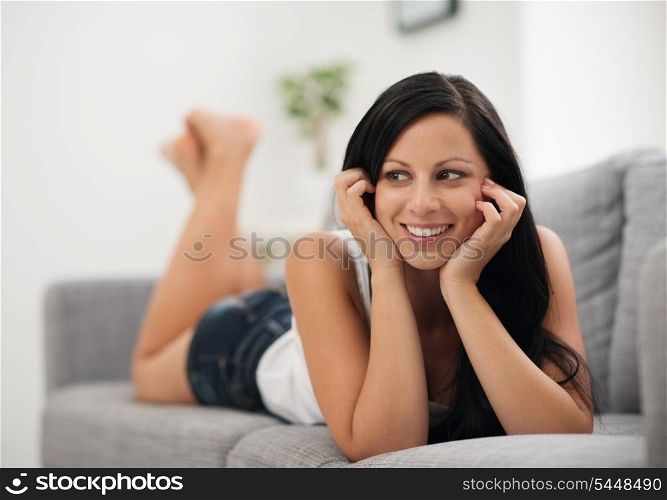 Portrait of happy young woman laying on sofa and looking on copy space