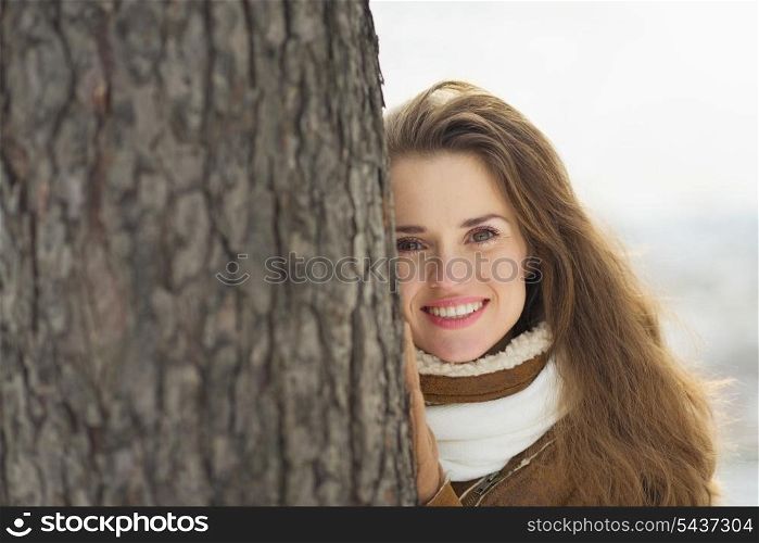 Portrait of happy young woman leaning against tree in winter park