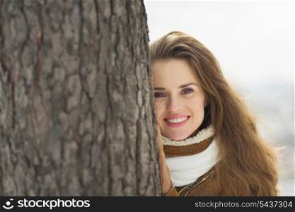 Portrait of happy young woman leaning against tree in winter park