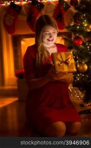 Portrait of happy young woman looking inside Christmas gift box at night