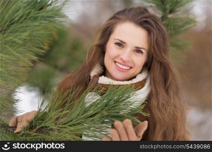 Portrait of happy young woman near spruce in winter outdoors