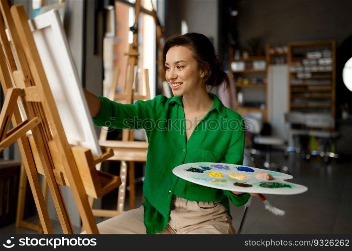 Portrait of happy young woman painting brush on canvas at workshop during art lesson class. Creative leisure activity concept. Portrait of woman painting brush on canvas at workshop during art lesson class